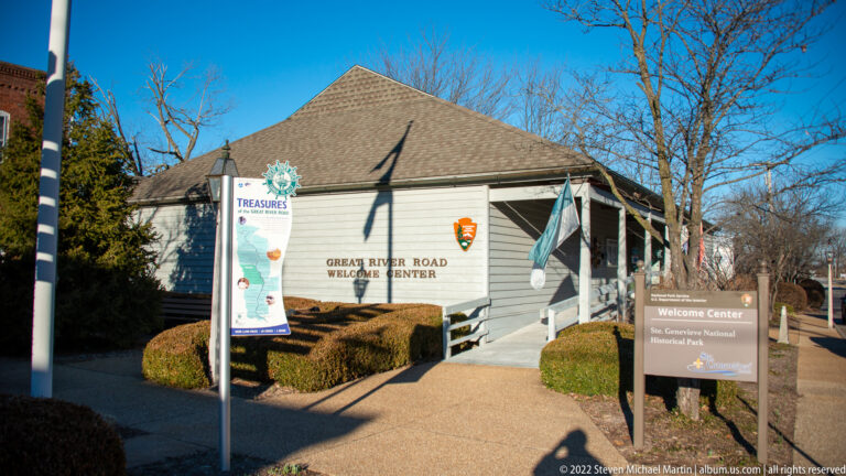 A low visitor center bears the Great River Road name beside an NPS sign and clipped hedges.