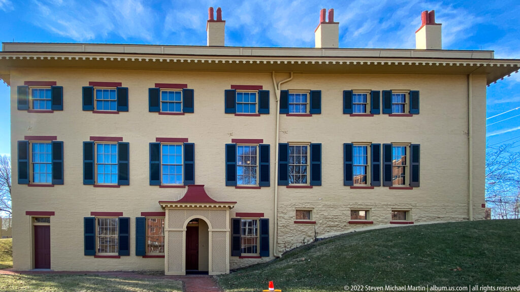 The Taft family home has a pale brick facade, dark shutters, red lintels, and a small entrance portico.