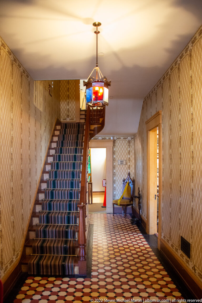 A carpeted staircase rises beside patterned wallpaper above a geometric tile floor.