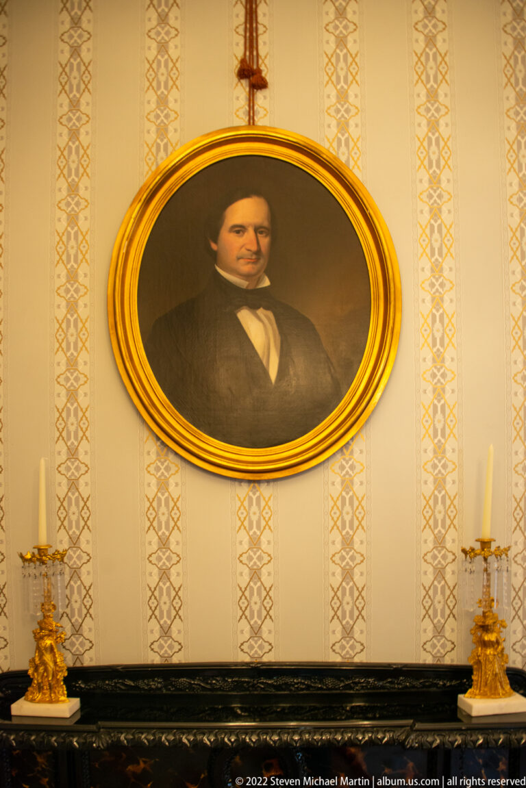 An oval portrait of a man hangs above a black mantel with gilded candlesticks.