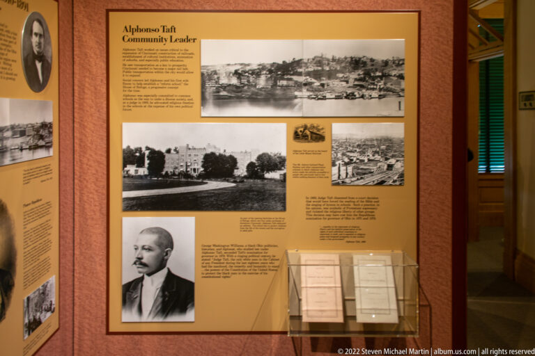 An exhibit panel combines archival building photographs, a portrait, text, and framed documents.