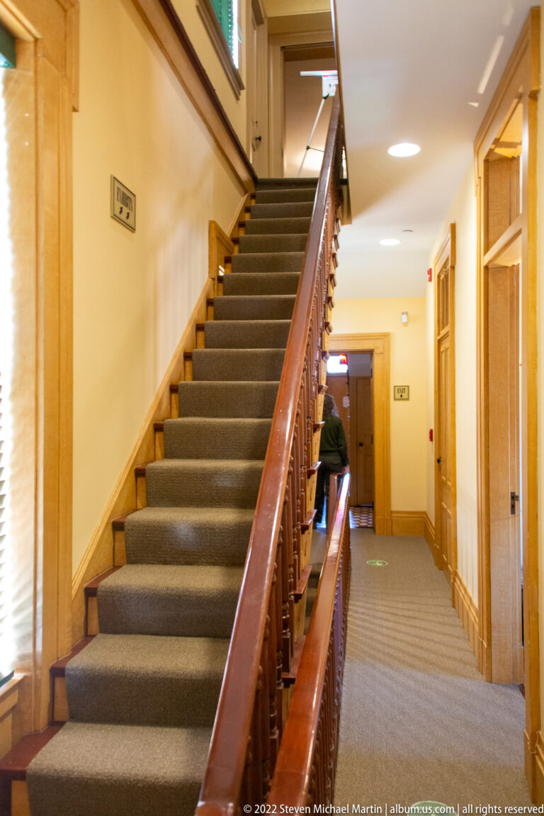 A carpeted staircase with a polished wood balustrade rises through the home’s central hall.