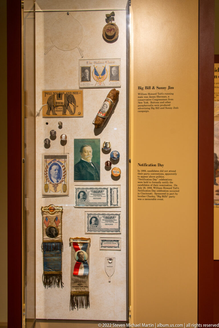 A display case contains campaign buttons, medals, ribbons, photographs, and printed memorabilia.