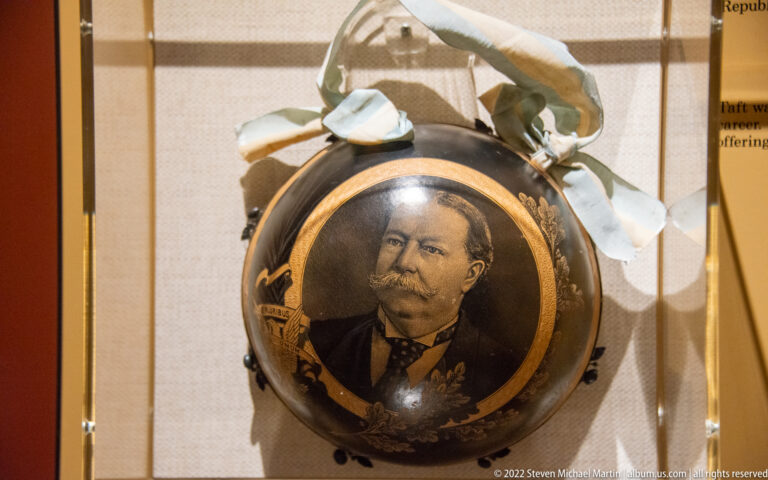 A round portrait of Taft is set in a dark decorated object beneath a pale bow and ribbons.