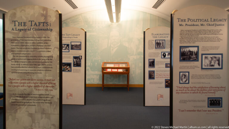 Freestanding panels about Taft’s legacy line a gallery around a central glass display case.