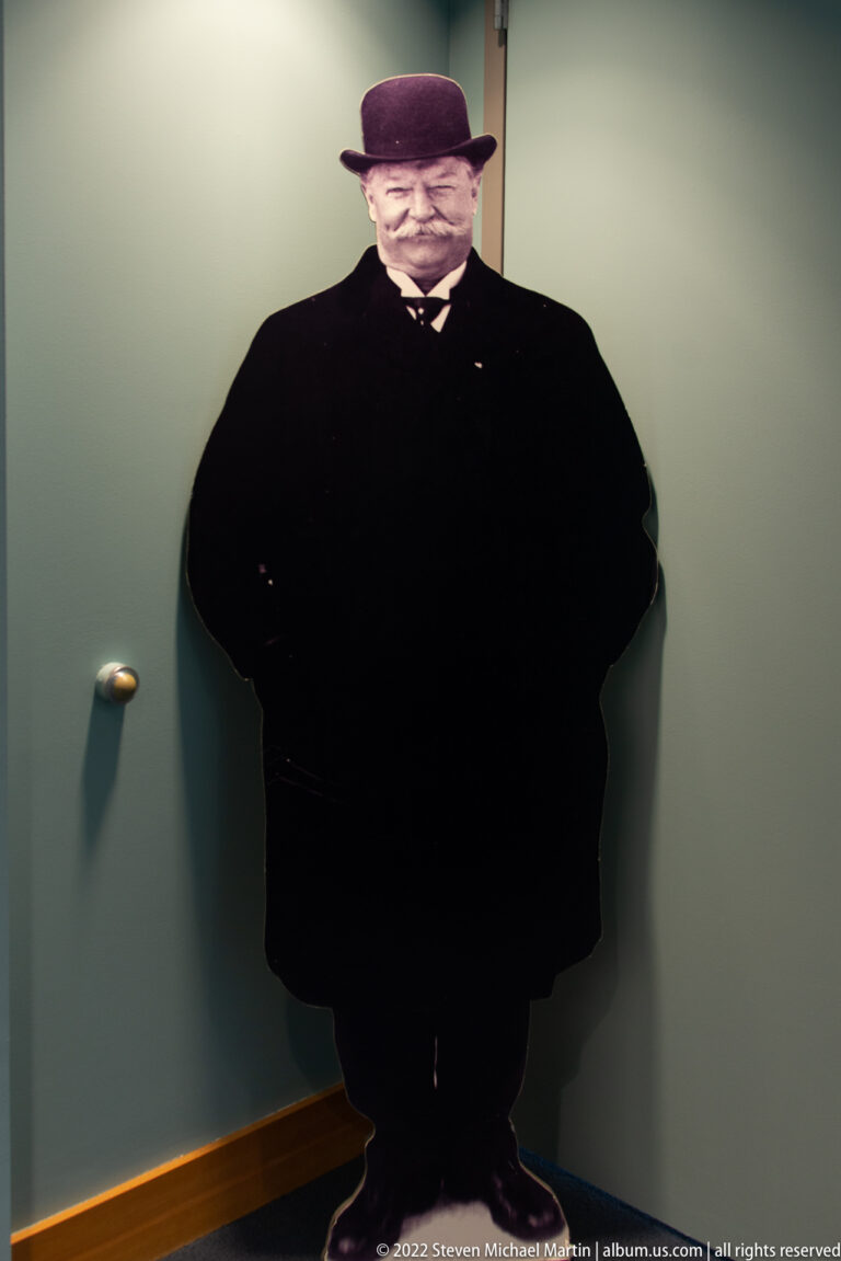 A life-size figure of Taft wears a dark suit and bowler hat against a pale green wall.