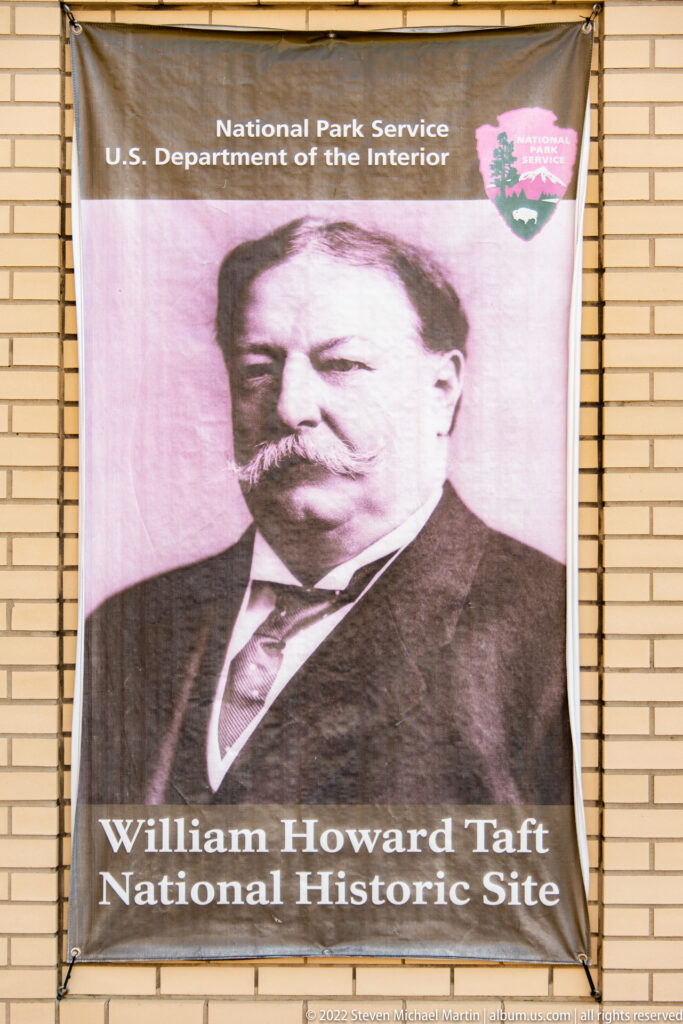A banner with William Howard Taft’s portrait and the site name hangs on a brick wall.
