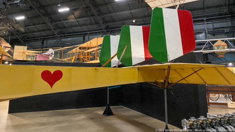 A yellow biplane with a red heart and green-white-red tail stands among other aircraft.
