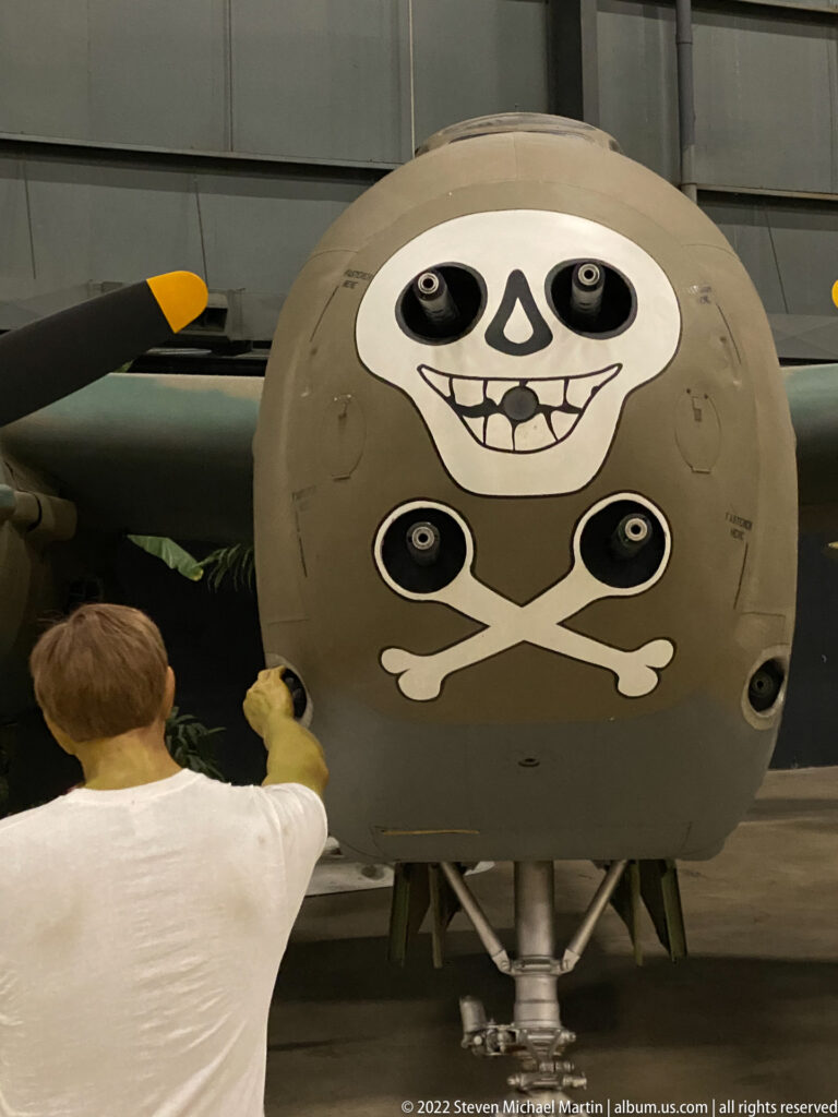 A visitor stands beside an aircraft nose painted with a skull and crossed bones.