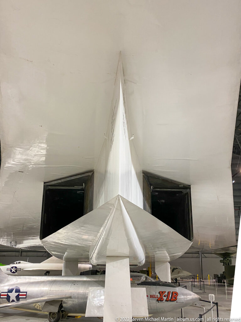 A broad aircraft tail is seen from below above other planes in the museum gallery.