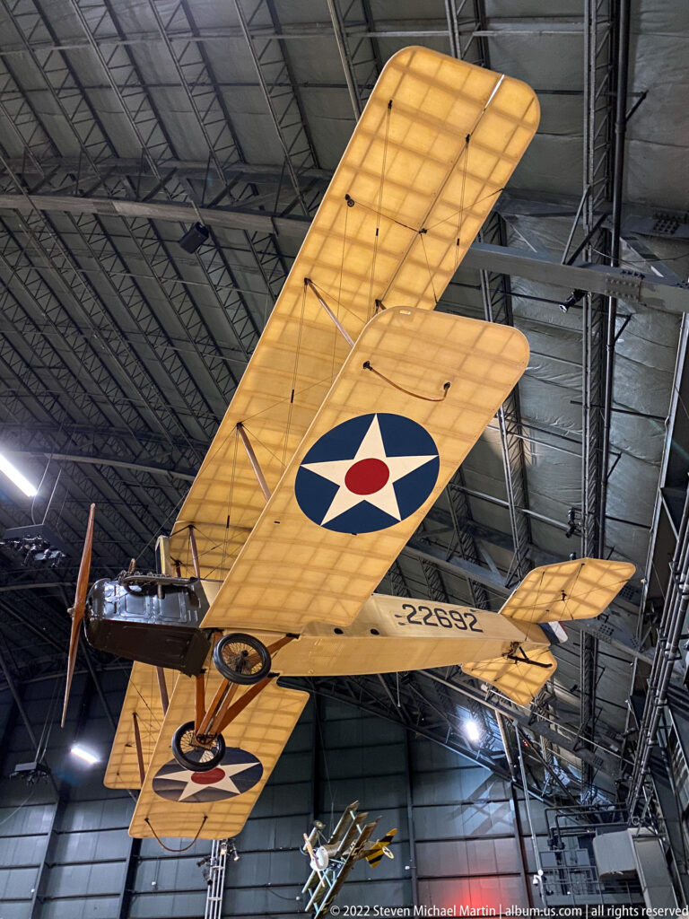 A yellow biplane’s lower wing bears a U.S. roundel, with struts and wires visible overhead.