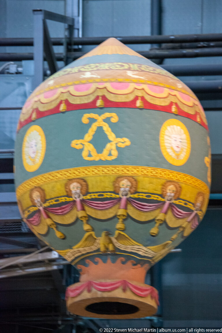 A rounded fabric envelope bears green, pink, and gold bands with figures and circular medallions.