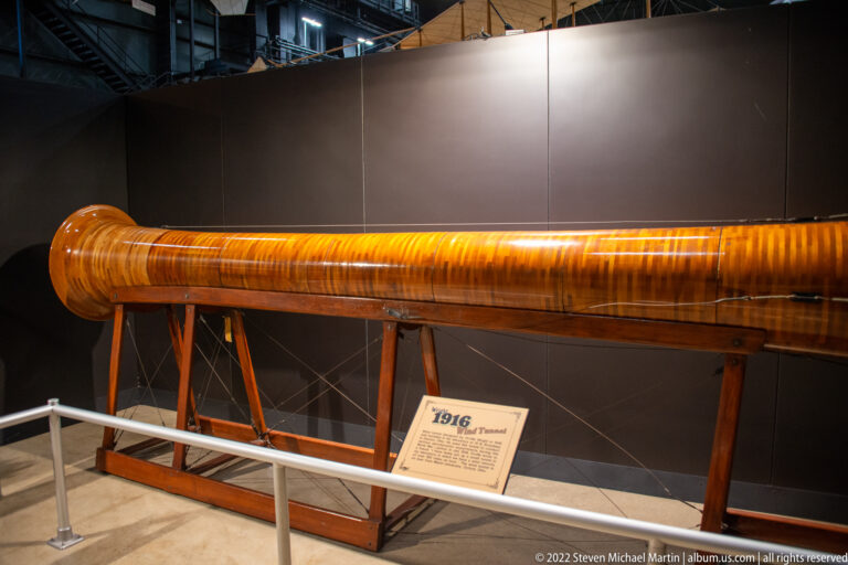 A long polished wooden aircraft propeller rests horizontally on a low timber stand behind a rail.