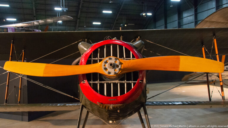 An orange wooden propeller crosses a red circular aircraft nose, with internal bars visible behind the hub.