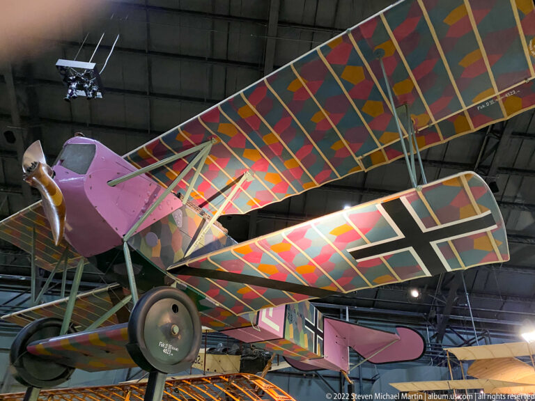 A pink-nosed biplane has brightly colored geometric panels across its stacked wings.