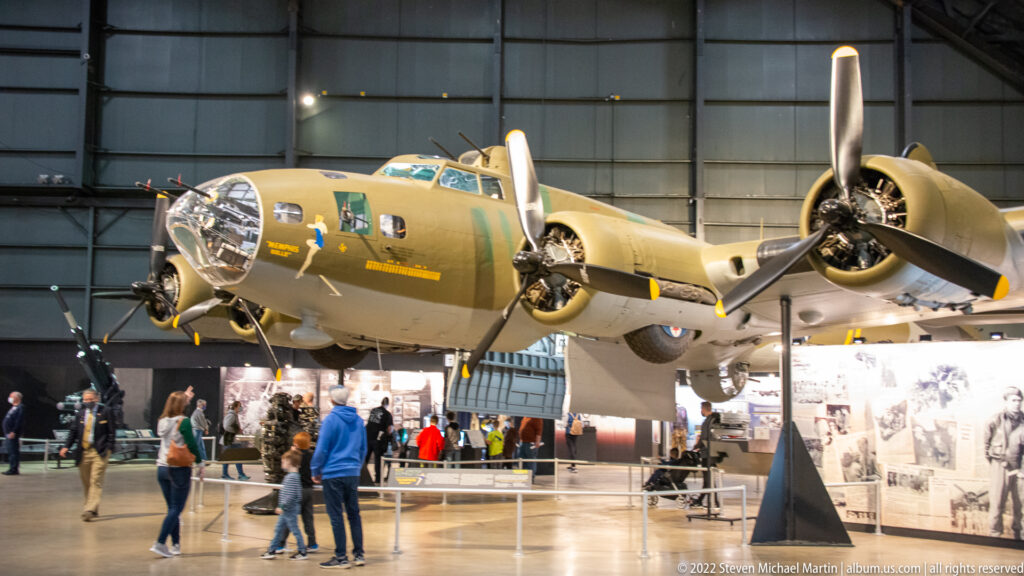 A large B-17 bomber hangs over visitors, with its glazed nose and broad wing spanning the gallery.