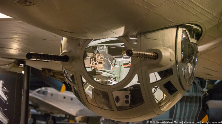 A spherical glazed ball turret with two gun barrels projects from the underside of a bomber.