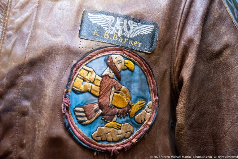 A blue name patch reading E. B. Barhey sits above a circular embroidered aviation emblem on leather.
