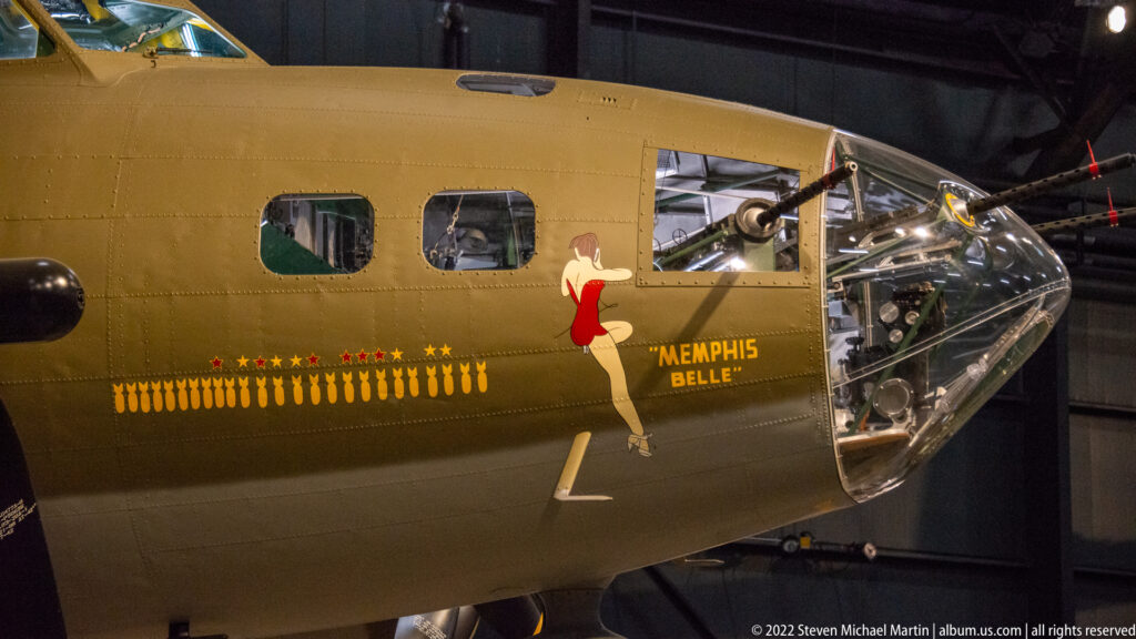 The B-17 Memphis Belle nose bears pin-up artwork, mission symbols, and clear bombardier glazing.