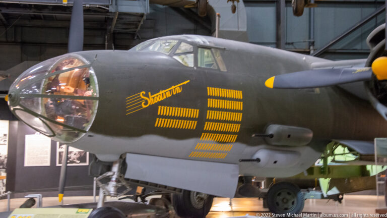 The rounded glass nose of Shady Lady sits beside yellow lettering and mission tallies on a dark fuselage.
