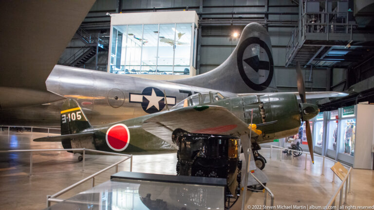 A silver aircraft with a U.S. star stands behind an olive aircraft marked with a red roundel and number 3105.