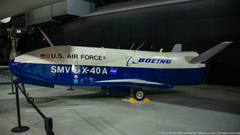 The Boeing X-40A sits on landing gear with U.S. Air Force, Boeing, and SMV X-40A markings visible on its white and blue body.