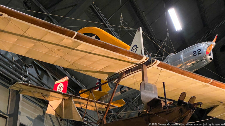 Tan biplane wings and struts overlap several aircraft, including a silver plane marked 22.