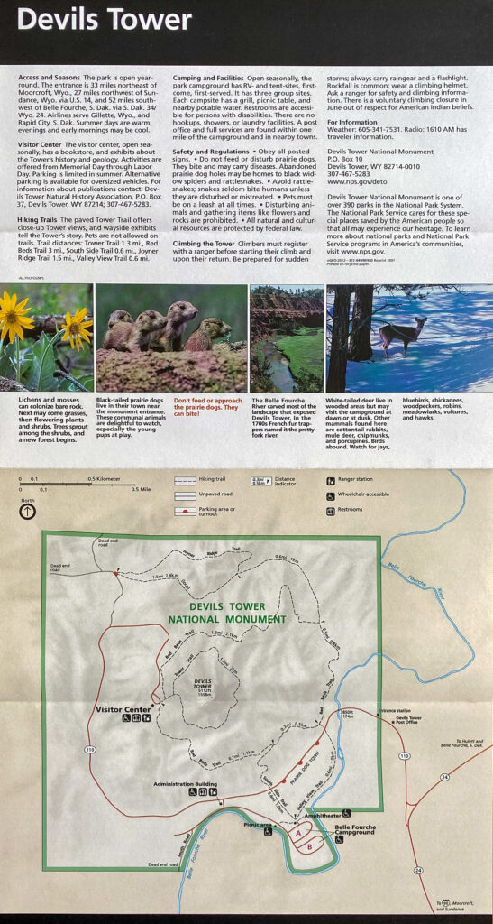 A Devils Tower National Monument sign displays a trail and road map beneath text and photographs.