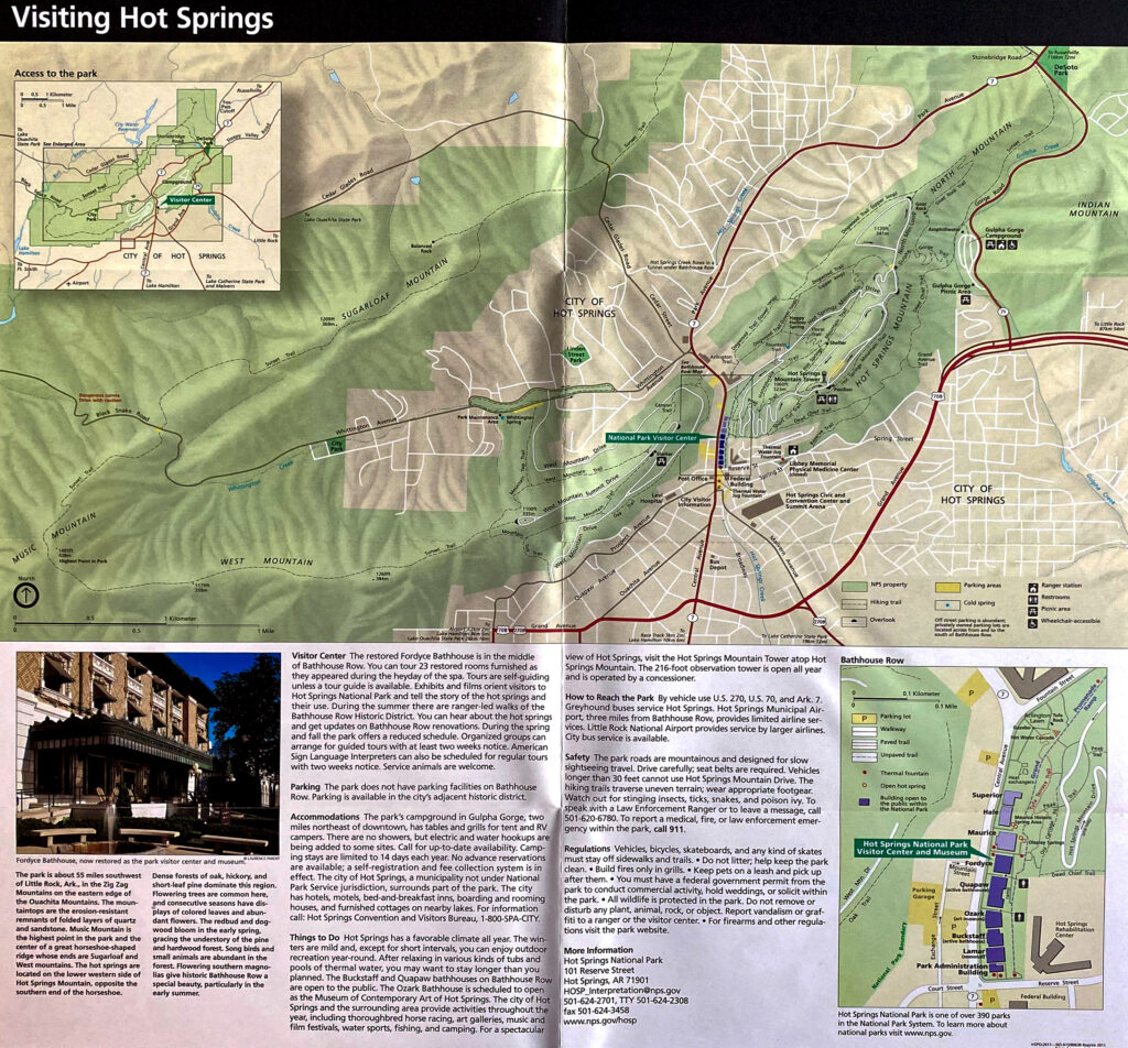 An open visitor guide displays a street map of Hot Springs with route lines, terrain shading, and smaller insets.