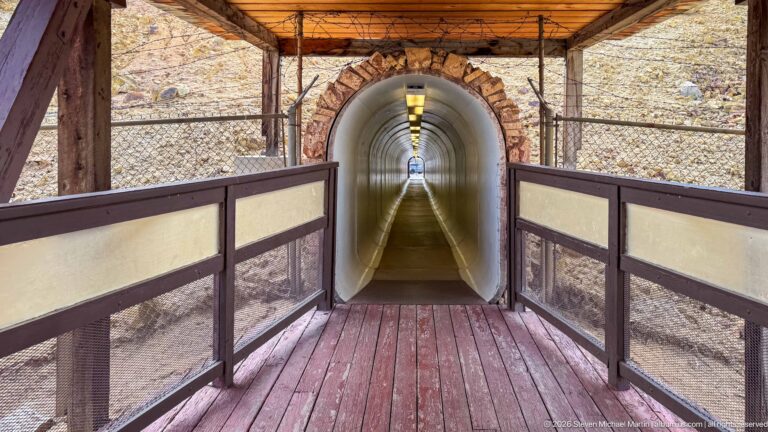 Long white pedestrian tunnel with ceiling lights, concrete walkway, and timber-framed entrance at the Berkeley Pit visitor site.