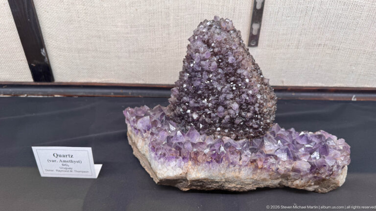 Dark purple amethyst crystal mound rising from a broader base of lighter lavender quartz crystals.