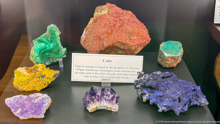 Assorted brightly colored mineral specimens arranged around an interpretive panel explaining mineral color.
