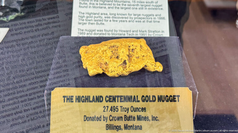 Large irregular gold nugget displayed above a plaque reading Highland Centennial Gold Nugget, 27.495 troy ounces.