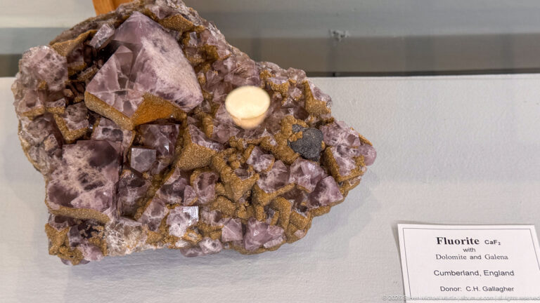 Purple cubic fluorite crystals with brown and pale associated minerals displayed beside a locality label.
