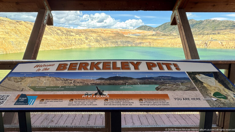 Large Berkeley Pit welcome panel in foreground with green pit water and terraced mine walls visible beyond.