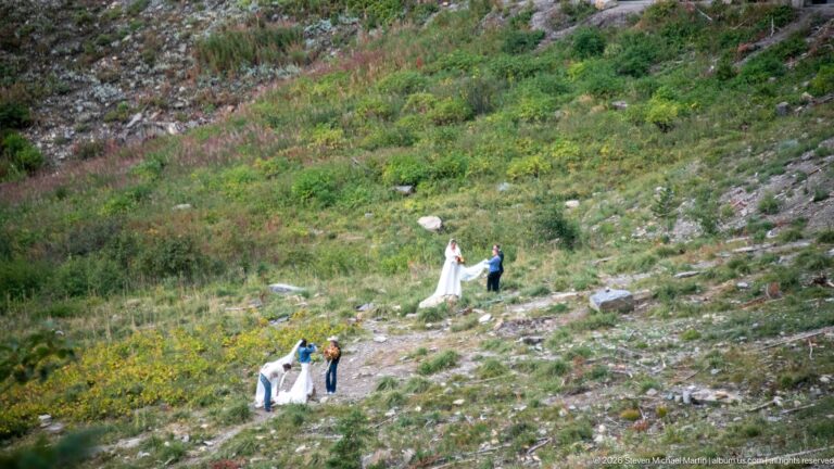 Several people stand on a rocky green mountainside with white fabric visible on the slope.