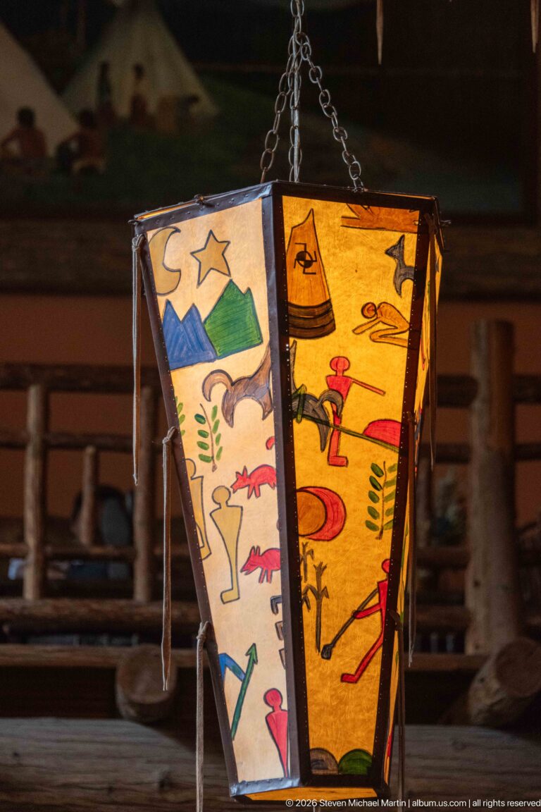 Close view of a glowing polygonal lantern painted with mountains, stars, plants, birds, animals, and human figures.