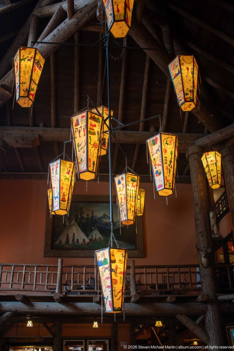Multiple brightly painted hanging lanterns suspended from the dark timber ceiling above the lodge lobby and gallery.