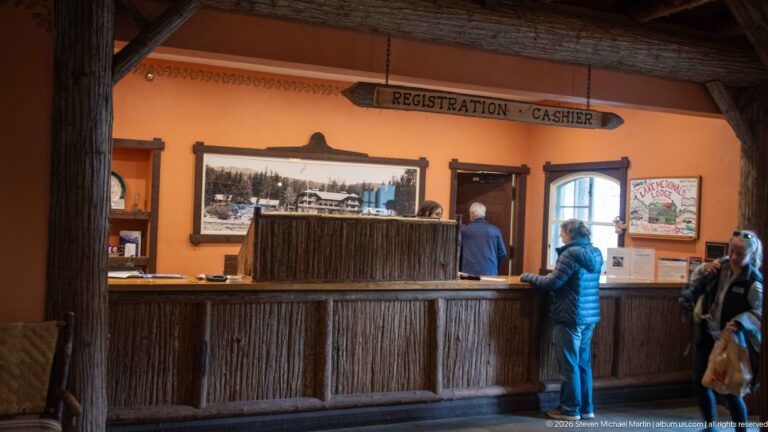 Guests stand at a rustic wooden registration counter beneath a carved Registration–Cashier sign in the lodge interior.
