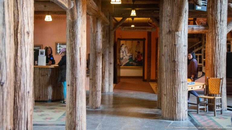 Interior passage framed by massive log columns with a hanging TELEPHONE sign, service counter, artwork, and seating.