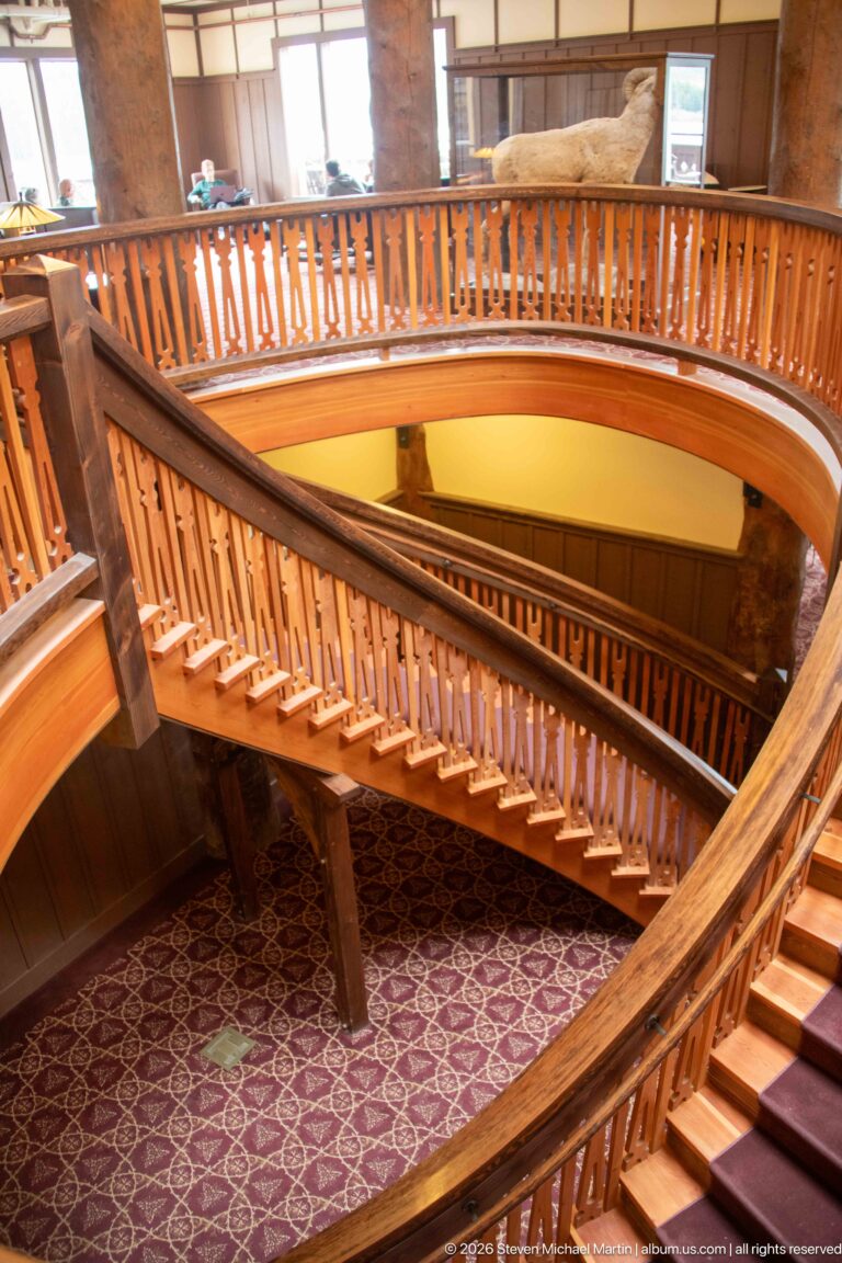 Curving multi-flight wooden staircase with polished railings and closely spaced balusters above patterned carpet.