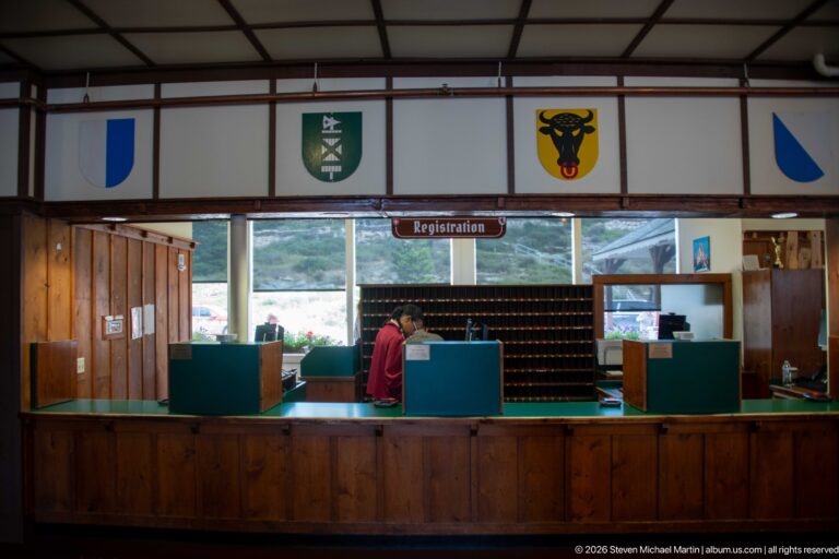 Registration desk with green counter partitions, staff member, wall of key slots, and heraldic shields overhead.