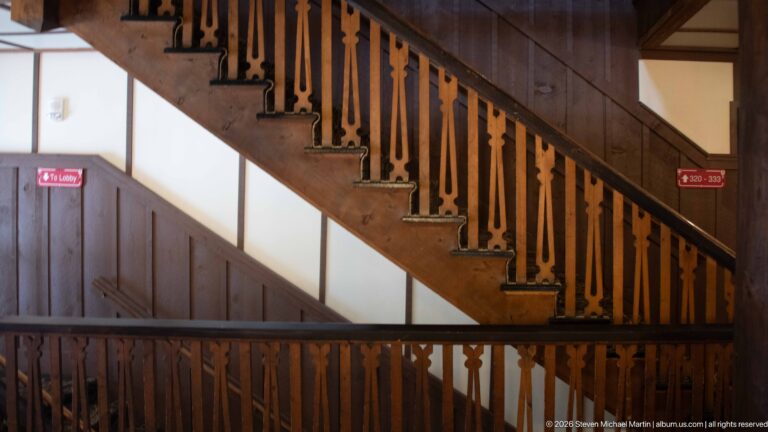 Wooden staircase with rustic balustrade above a landing marked by red lobby and room-direction signs.