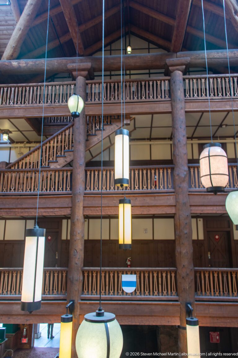 Three levels of wooden balcony railings between massive log columns, with large hanging lanterns in the foreground.