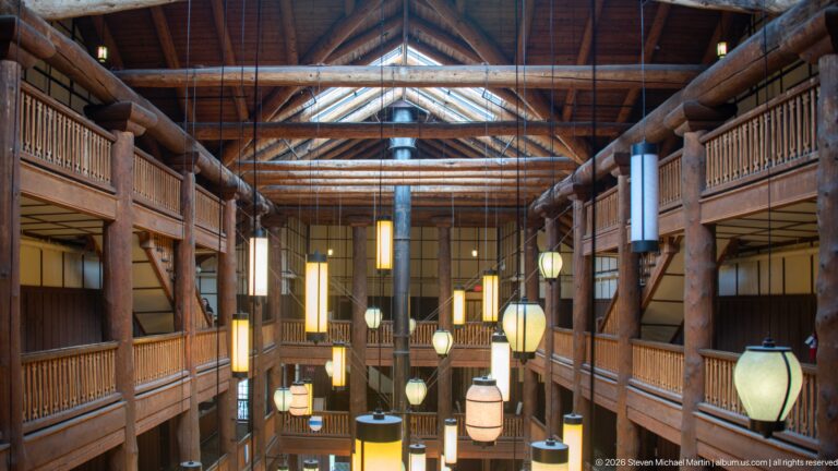 Upper-level view through the Great Room with log balconies, tall columns, roof framing, and suspended lanterns.