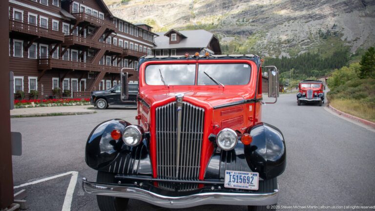 Front view of a red Glacier National Park touring bus with chrome grille outside Many Glacier Hotel.