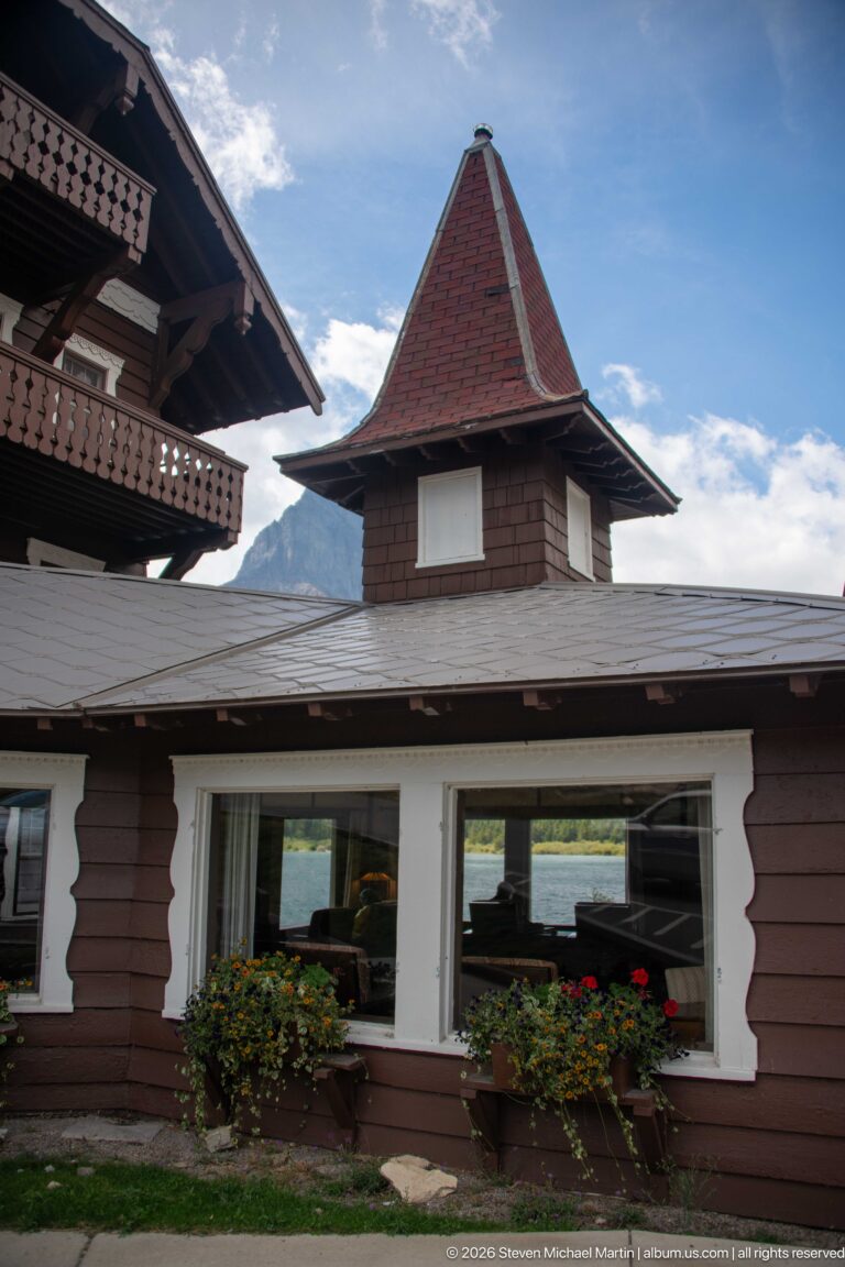 Low brown lodge wing with white-trimmed windows, flower boxes, and a small red pyramidal-roofed tower.