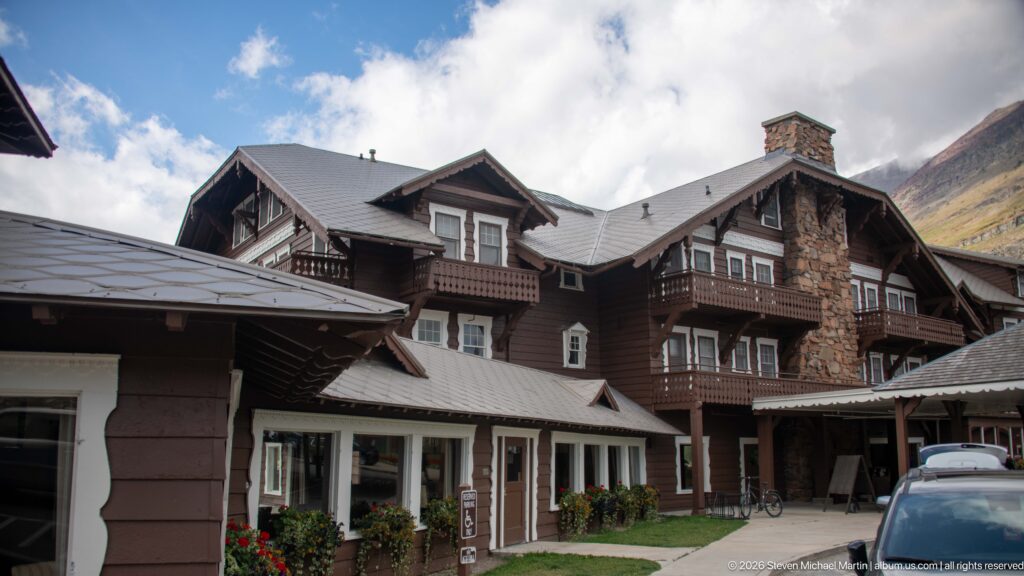 Multi-story brown lodge wings with balconies, dormers, stone chimney, and a small courtyard below.