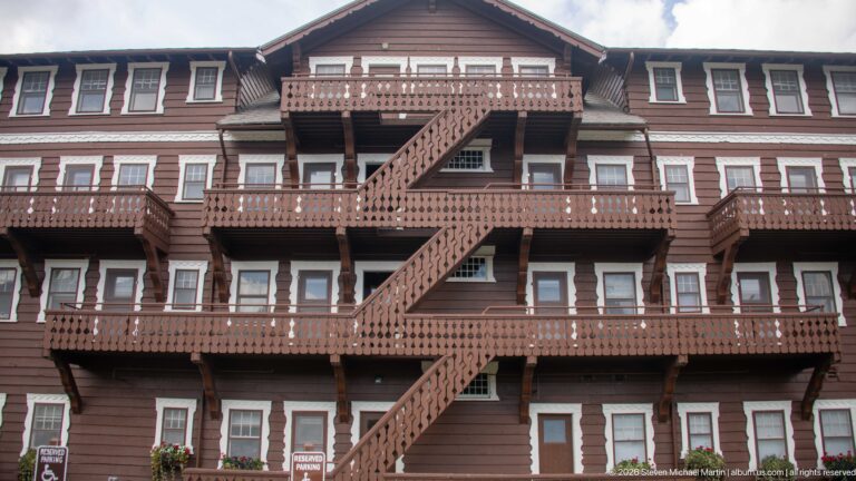 Zigzagging wooden exterior staircase crossing several balcony levels on the brown, white-trimmed hotel façade.