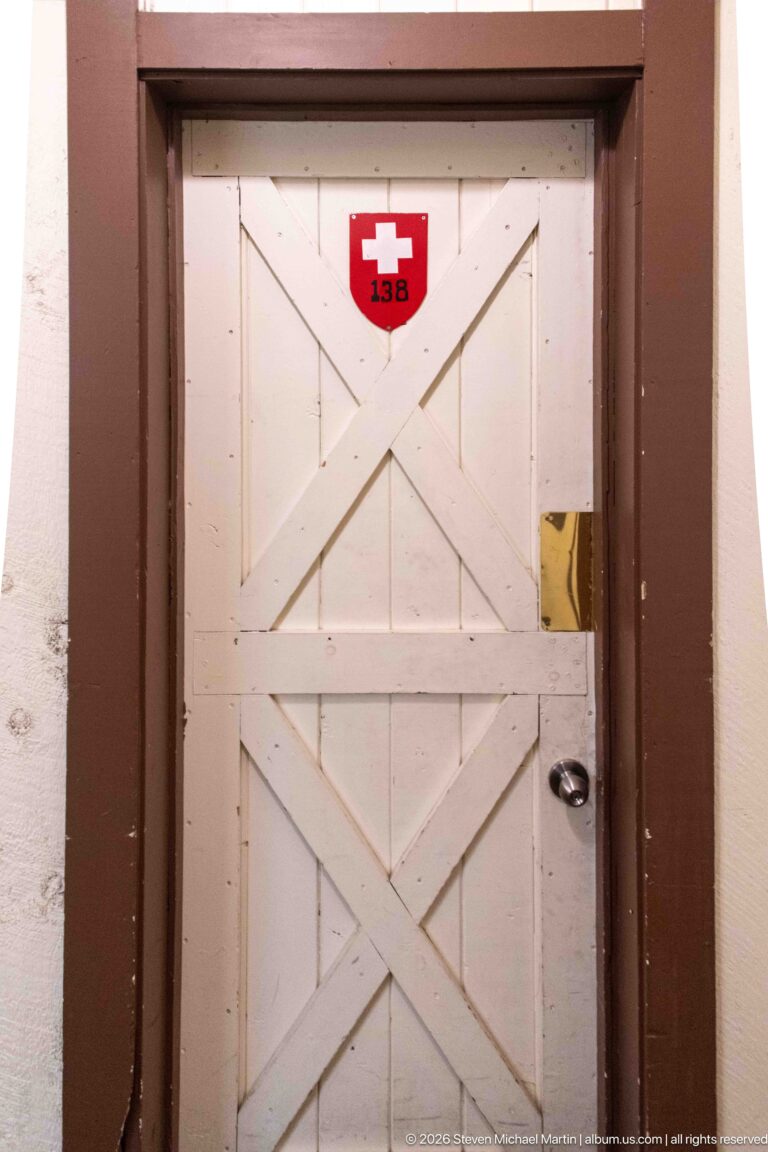 White cross-braced door with dark trim and a red Swiss-cross plaque marked 156 above it.